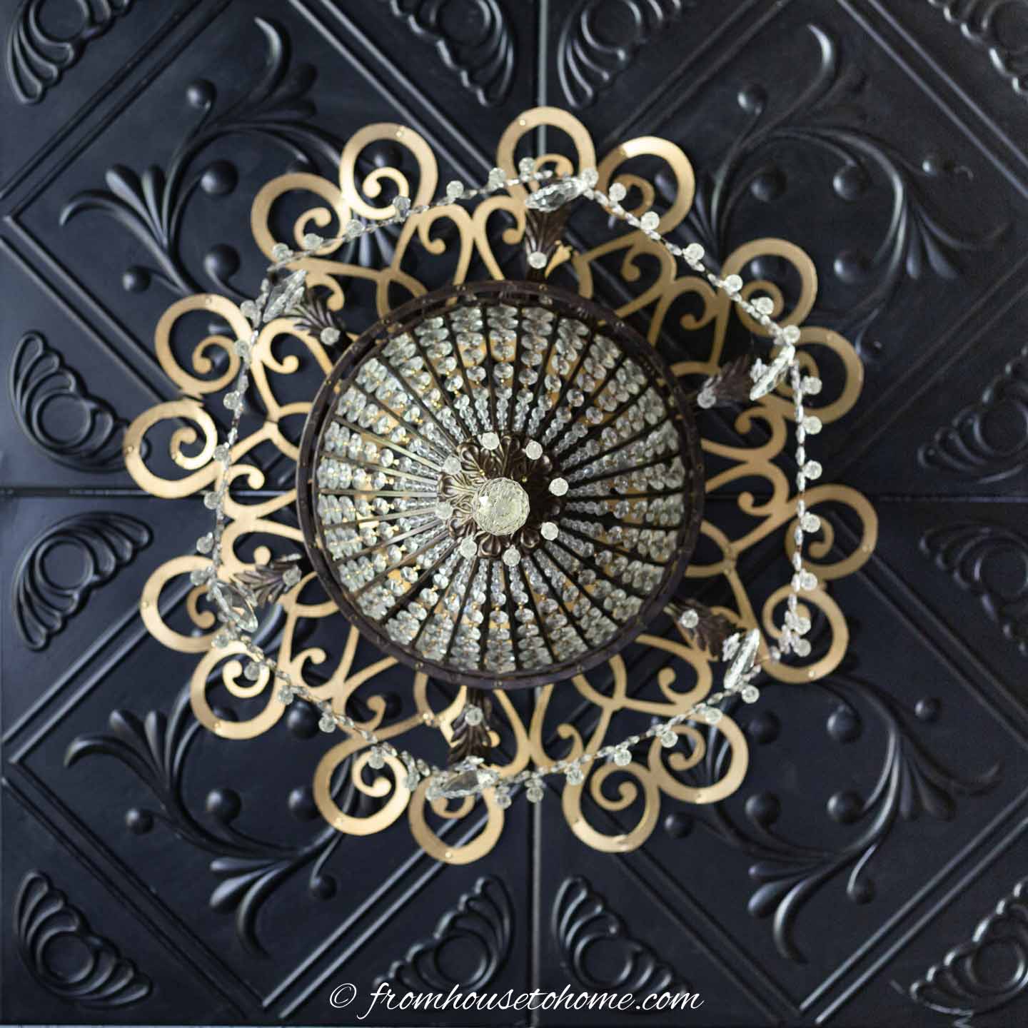 A DIY gold ceiling medallion around a chandelier on a ceiling that's painted black