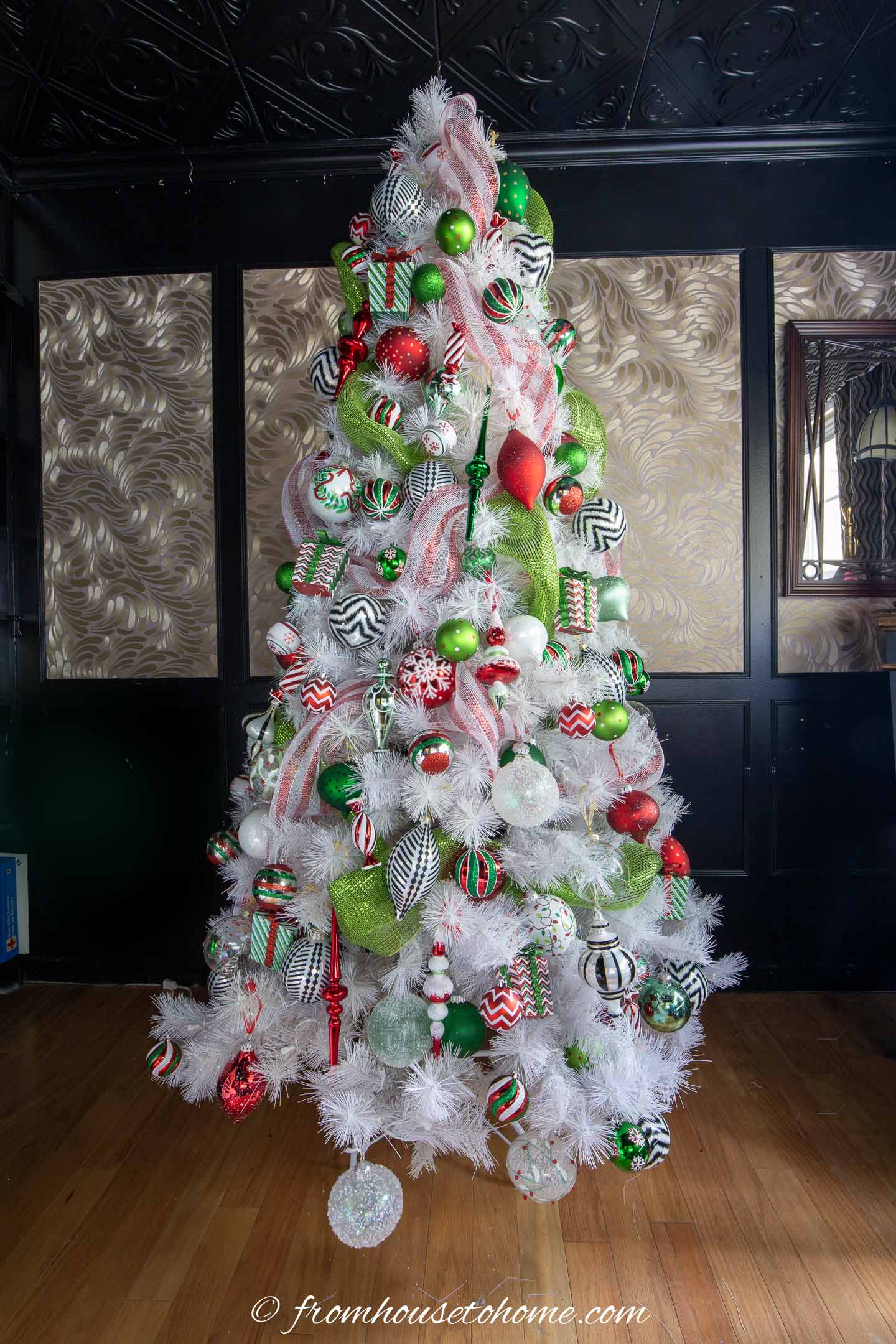 White Christmas tree with small and large green and red ornaments on it