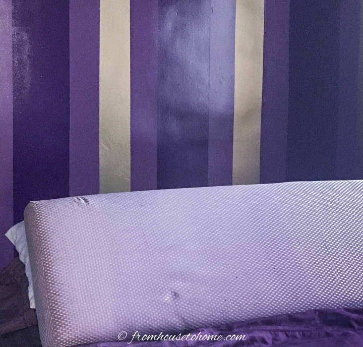 purple and gold striped wall behind the upholstered headboard