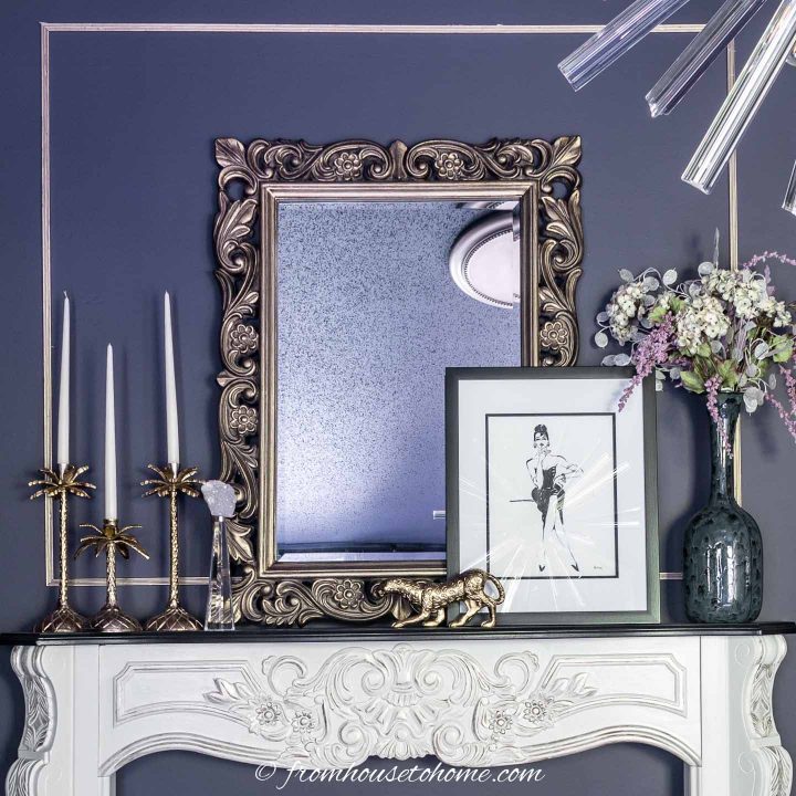 an intricate white mantle in front of a purple wall, with a large mirror sitting on top. 