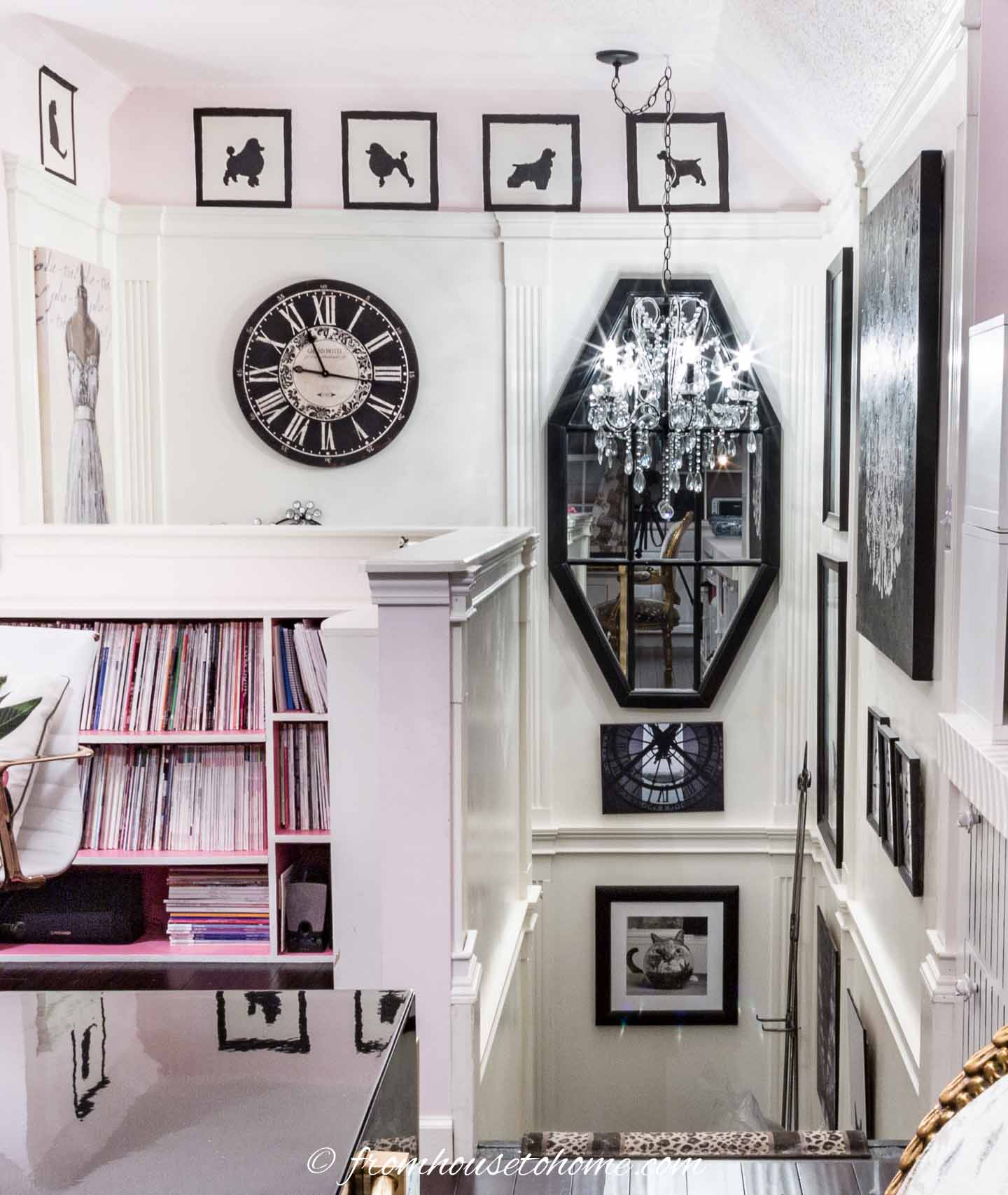 A large mirror hung on a stairwell gallery wall with black and white pictures