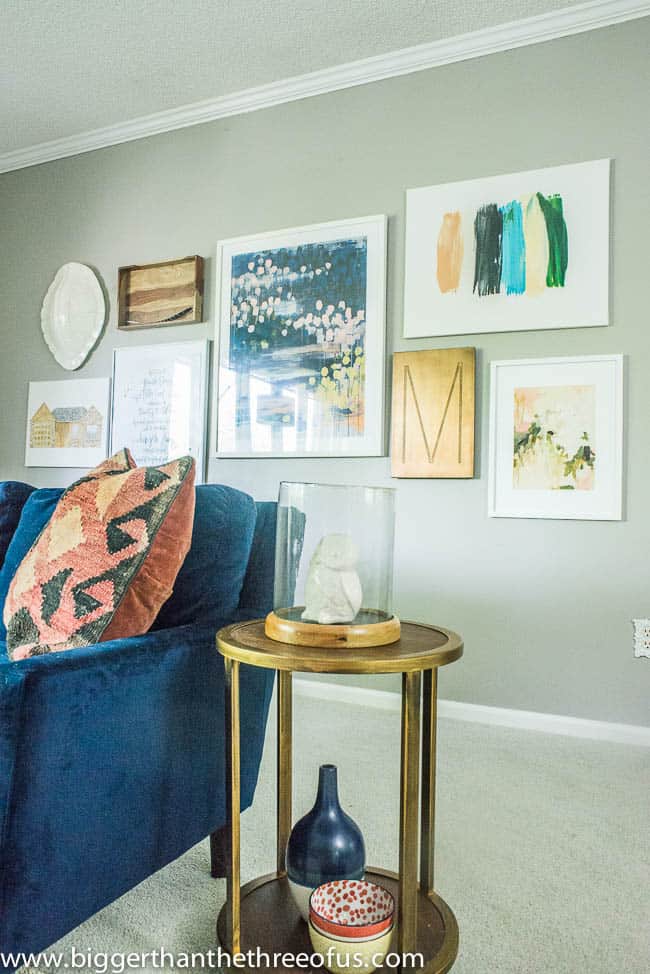 A gallery wall in a living room filled with framed art behind a blue couch and gold side table.