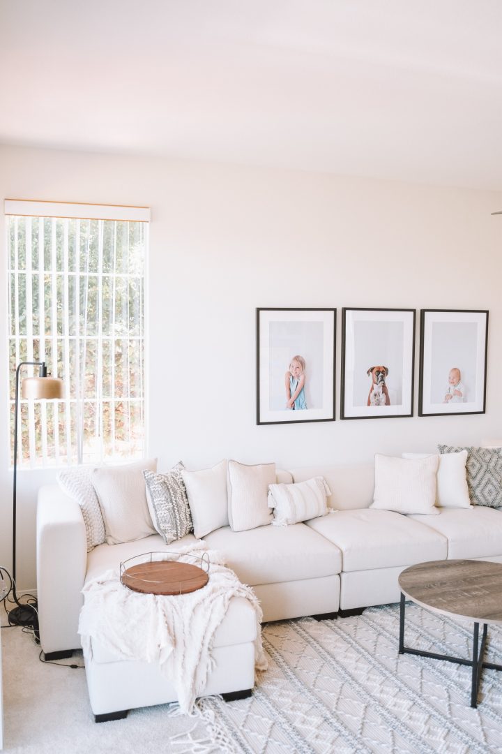 Oversized family photo prints in black frames on a large wall in a cozy living space.  