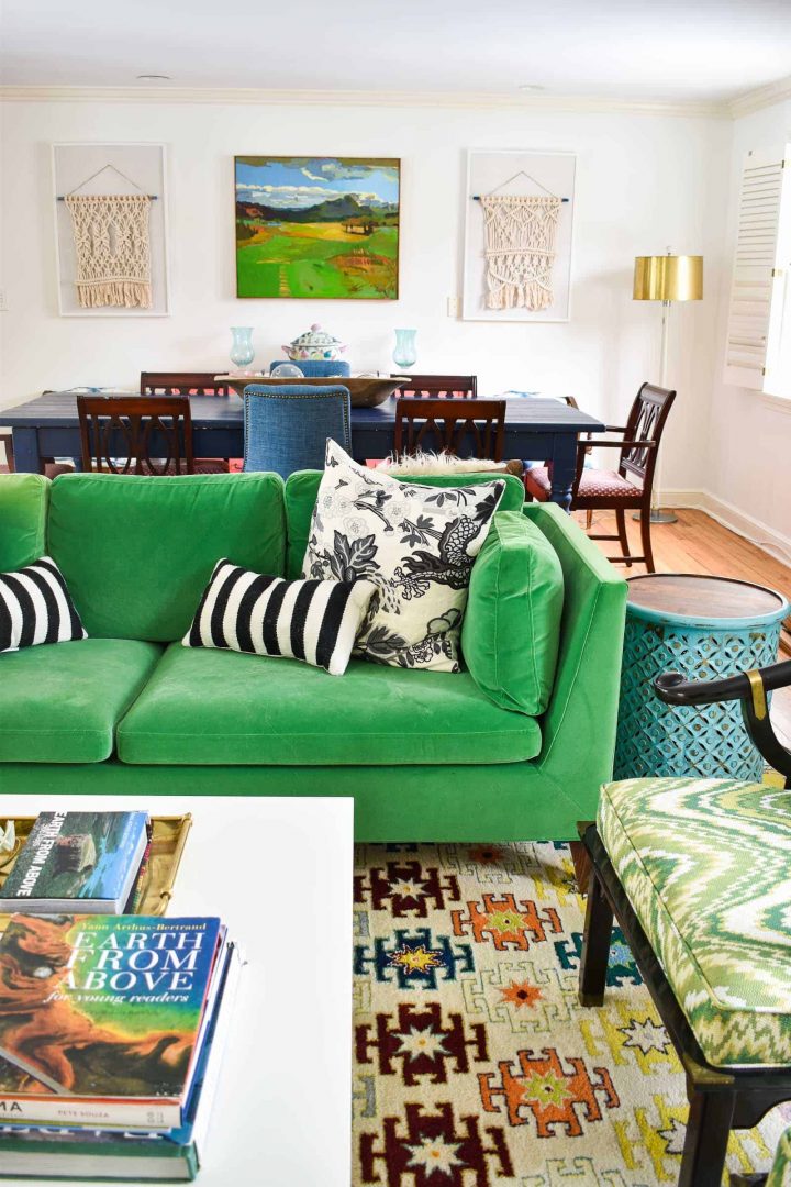 A bright green sofa with black and white throw pillows, with a decorated dining table in the background. 