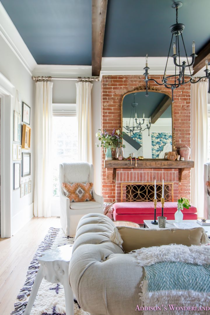 A brightly lit living space featuring a brick fireplace surround with an ornate mirror on the mantel.