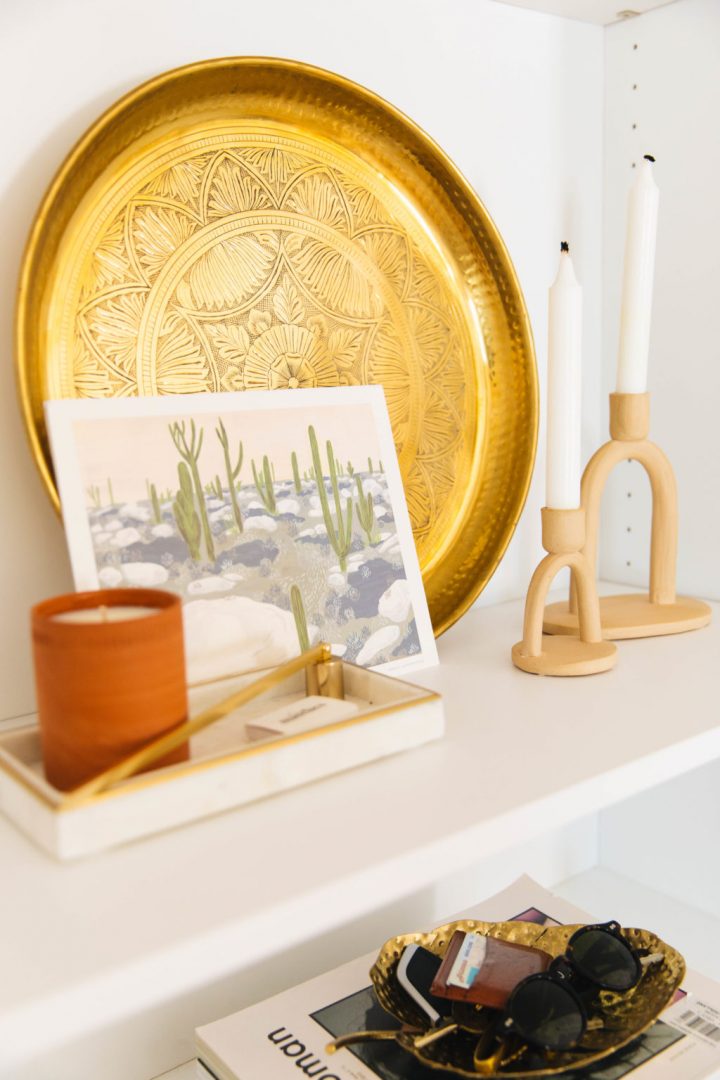 Bookshelf with gold tray, a postcard, pillar candle in a tray and wooden candlesticks