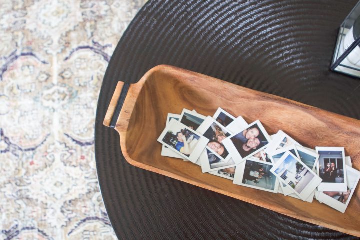 A wooden dough bowl filled with photographs, on a round, black table. 