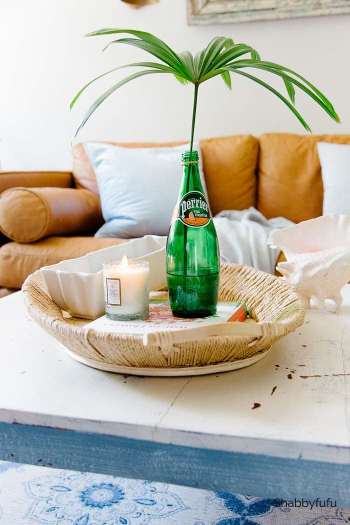 A basket filled with a candle, book and a glass bottle with a plant stem inside. 