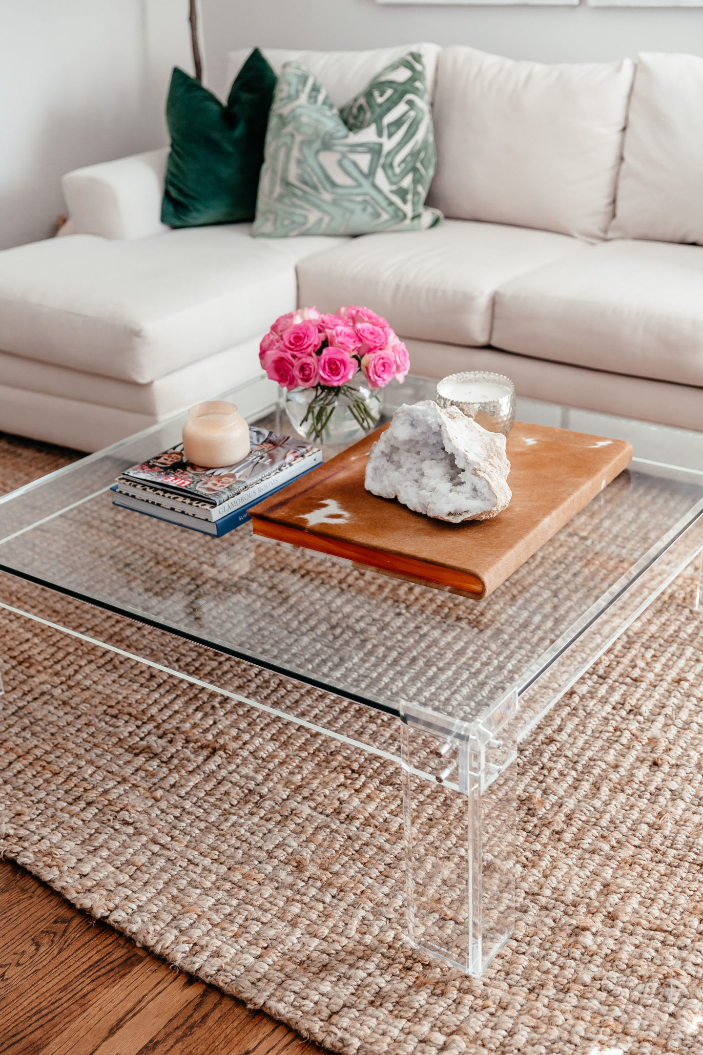 A square acrylic coffee table decorated with books, candles, some flowers and a geode