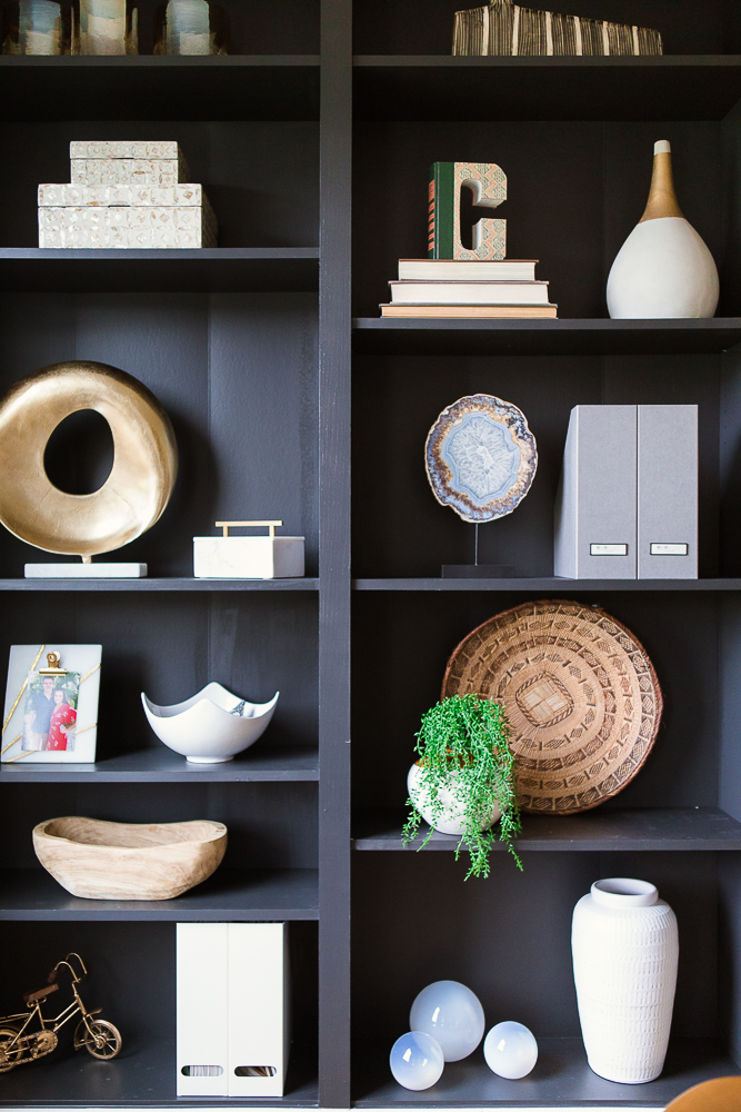 A black bookshelf styled with multiple round accessories and bowls