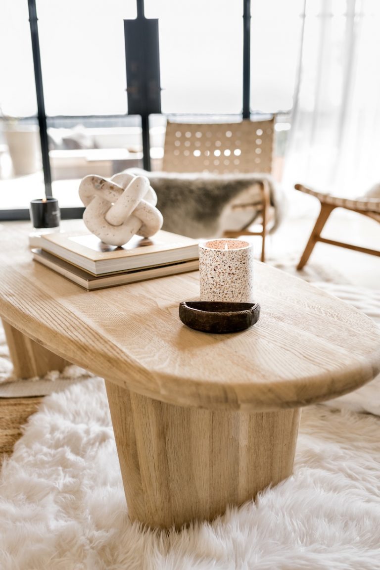 An oval coffee table styled with some books, a geometric object, and candles