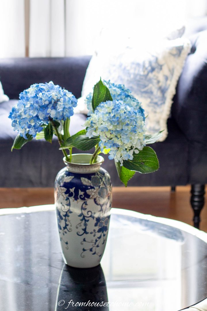 A ginger vase with blue hydrangeas on a round living room coffee table