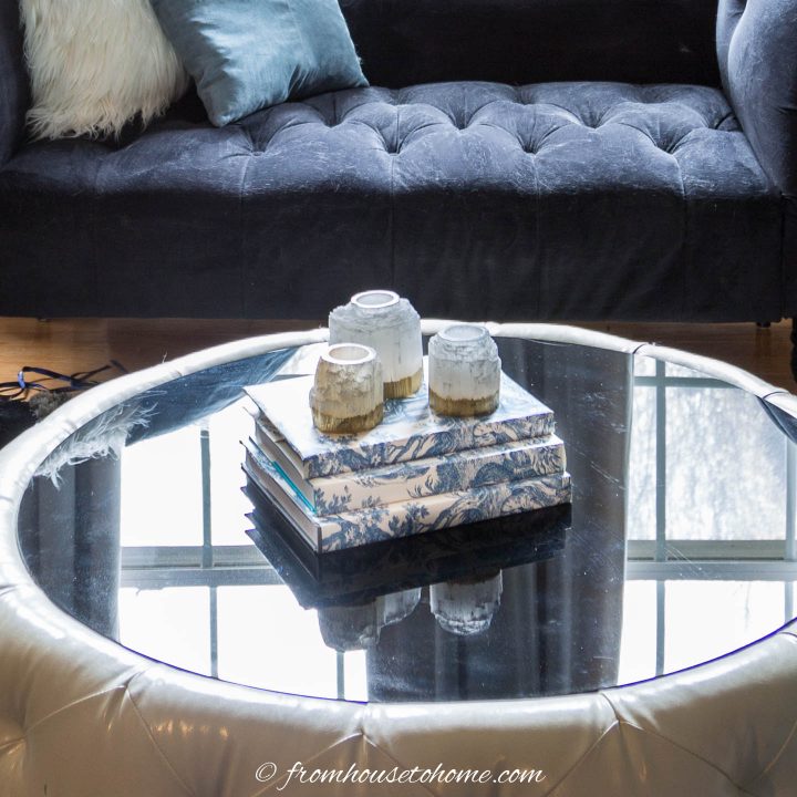 Three candles on a stack of books with blue and white wallpaper covers on a round coffee table