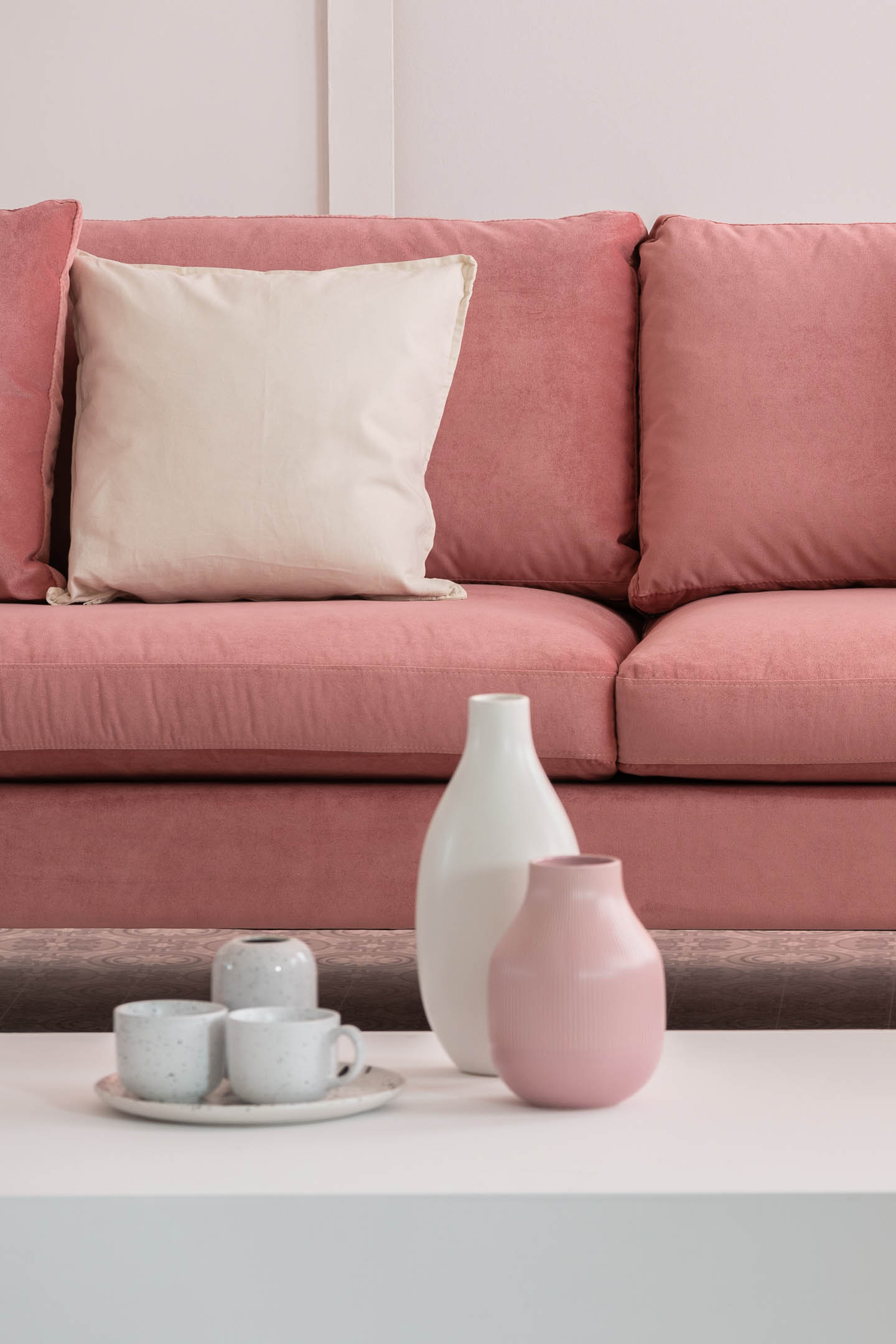 Pink and white vases arranged on a white coffee table in front of a pink sofa with white cushions