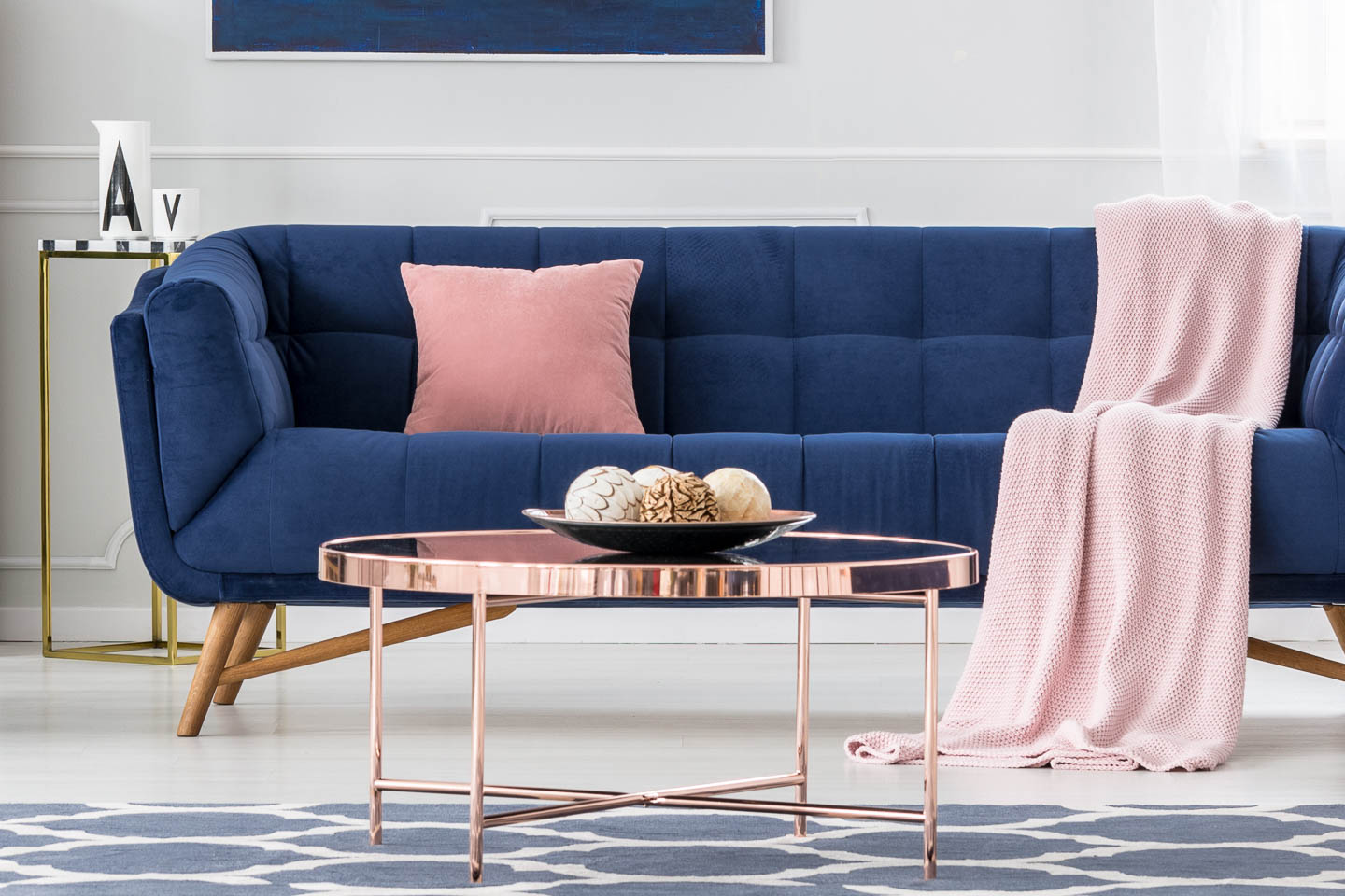Shallow bowl with round decorative objects on a rose gold coffee table in front of a blue sofa