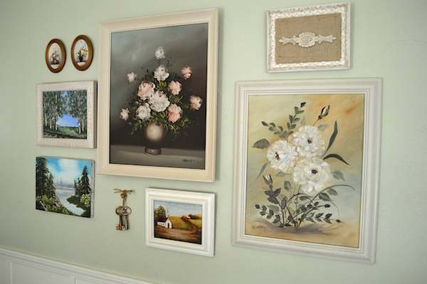 Oil paintings from a thrift store in a gallery style layout on a light green wall. 
