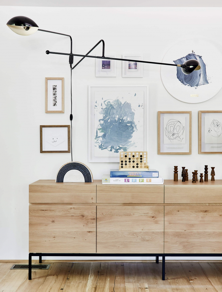Painted framed art on a white wall, above a wooden cabinet. 