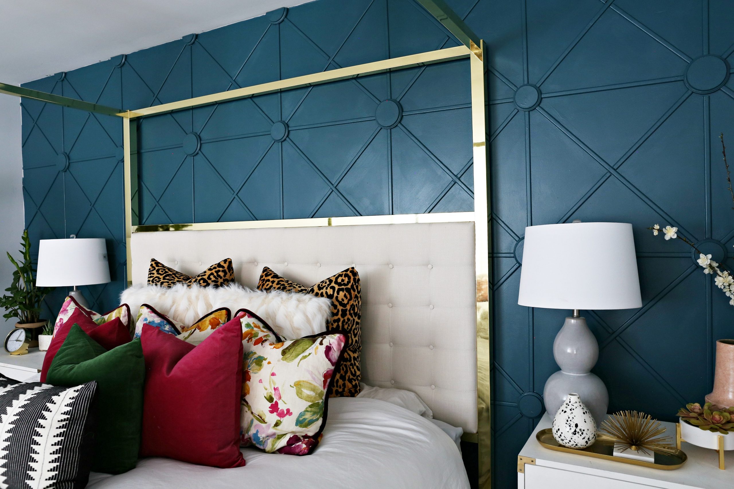 A wooden accent wall in a bedroom painted blue, behind a gold 4 post bed frame topped with colorful throw pillows. 