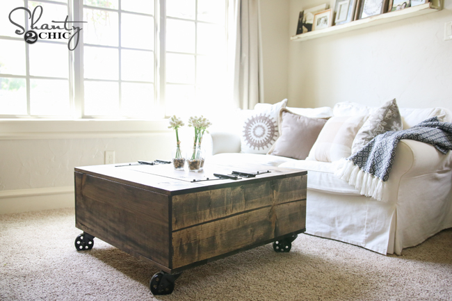 A DIY wooden coffee table on caster wheels in front of a white sofa. 