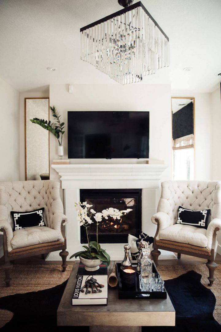 A fireplace with two mirrors on each side, a TV mounted over it and two accent chairs in front of it