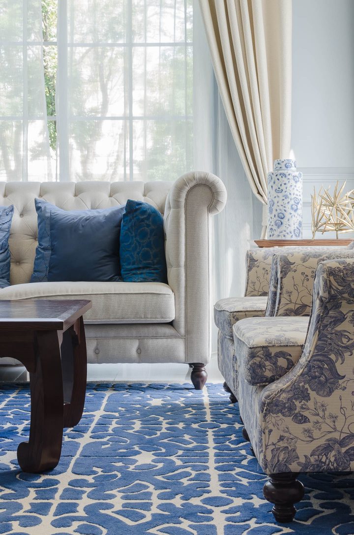 A blue and white living room with a sofa and two chairs that do not block the light from the window