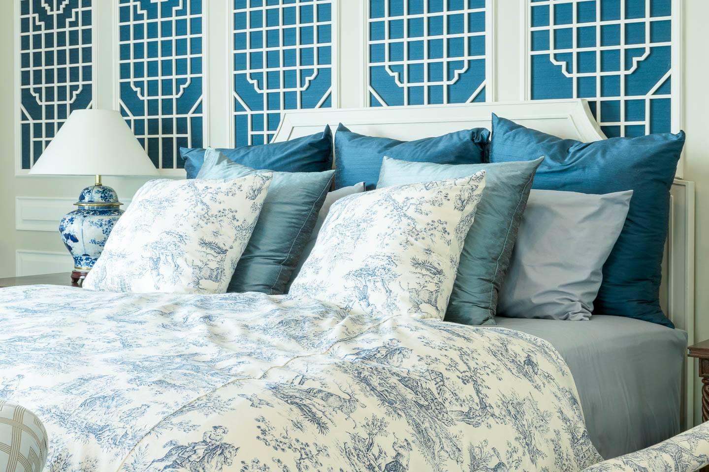 Bedroom with blue and white lattice panels behind a white bed frame with toile bedding
