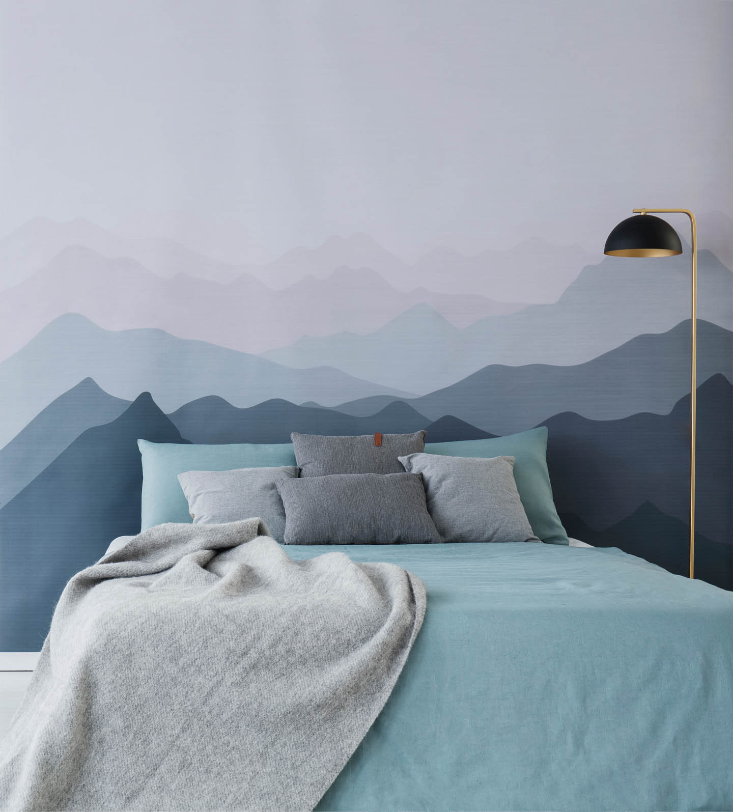 A mountain mural painted in blue behind a bed with aqua and gray bedding