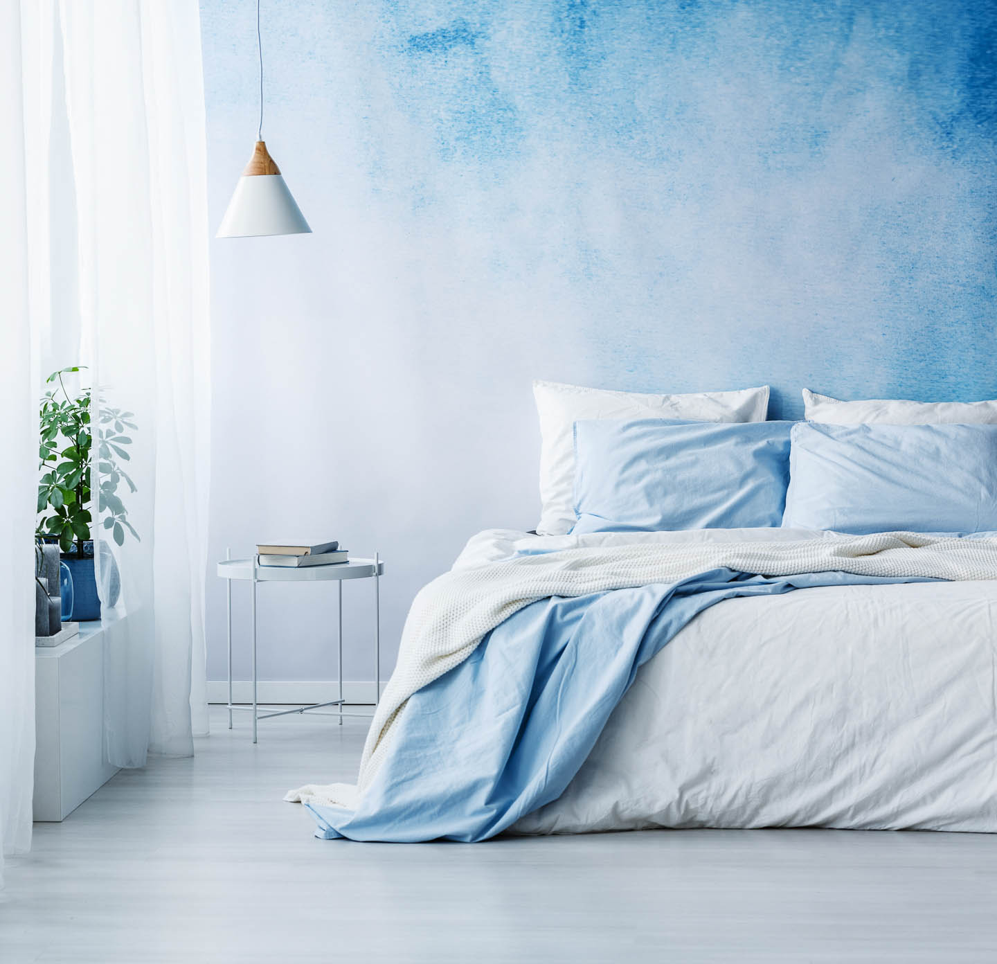 A bedroom with walls painted in an ombre blue pattern behind a bed with white and light blue bedding