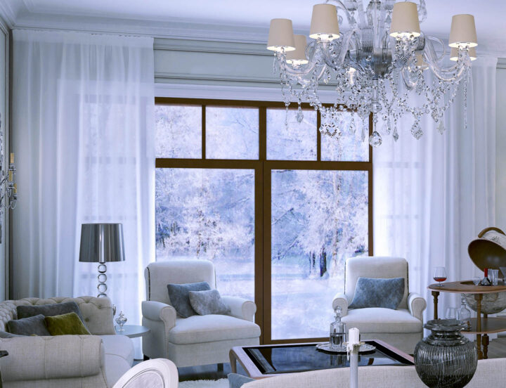 White curtains hung at the ceiling in a living room with two white chairs and a large chandelier