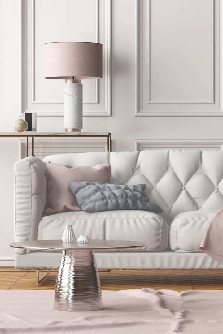 Round rose gold coffee table in front of a greige colored sofa with pink cushions 