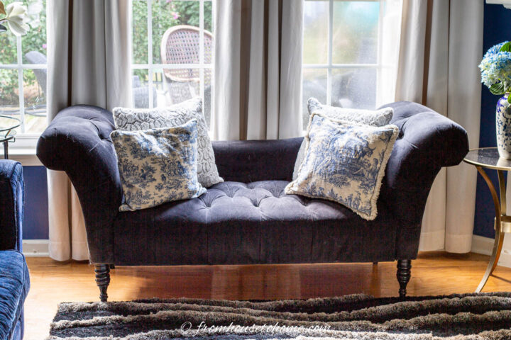A black settee with blue and white cushions in front of a window