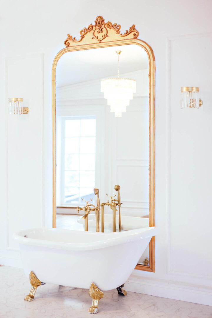 White bathroom with gold trim on a clawfoot tub and large mirror