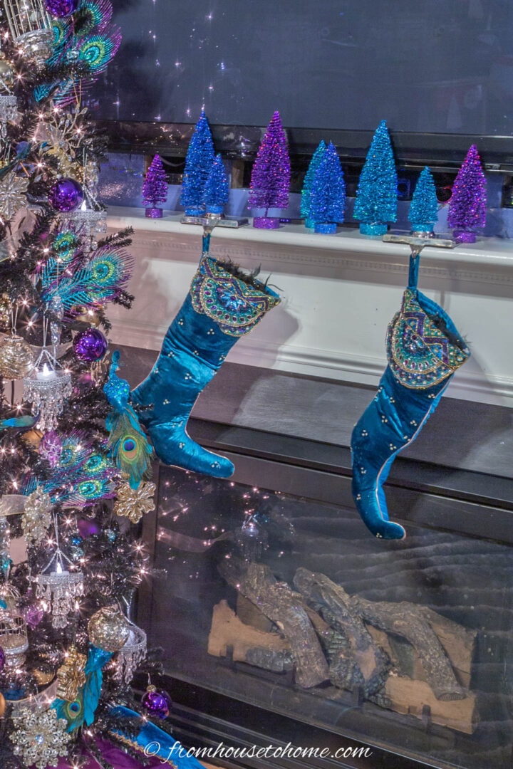 Fireplace mantel decorated for Christmas with blue and purple bottle brush trees above it and stockings