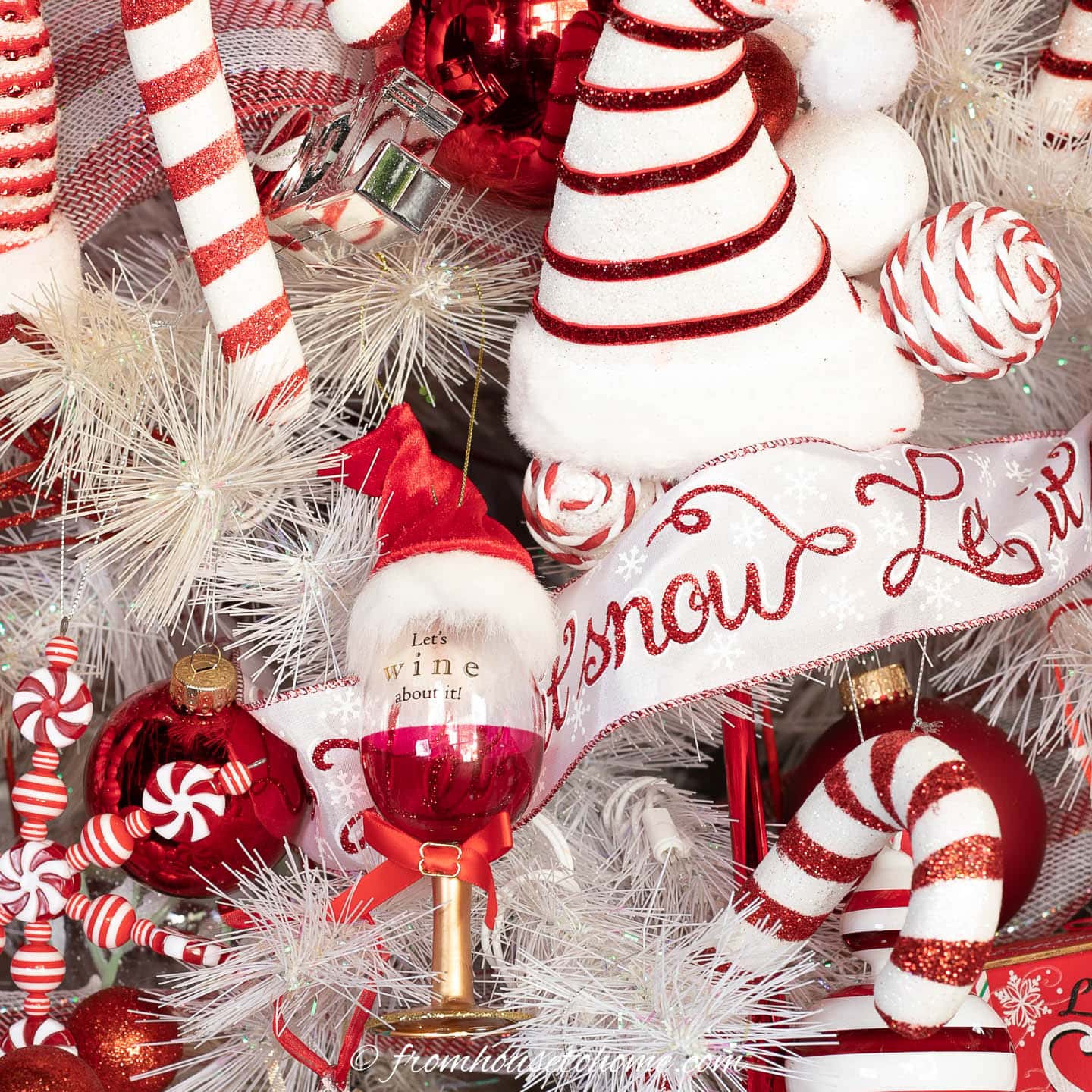 Santa wine glass , Santa hat and candy cane ornaments on a white Christmas tree wrapped with white and red ribbon