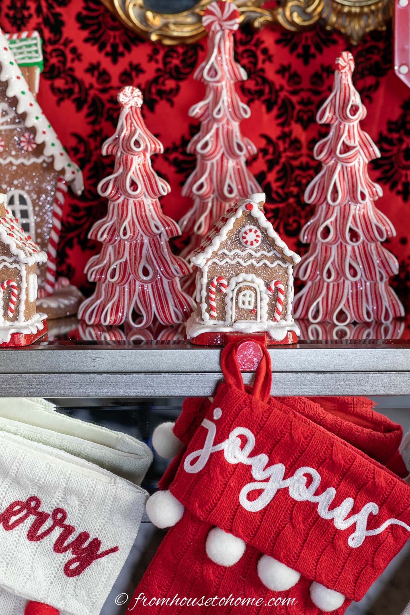 Gingerbread house stocking holder on a mantel in front of red and white tree Christmas decorations