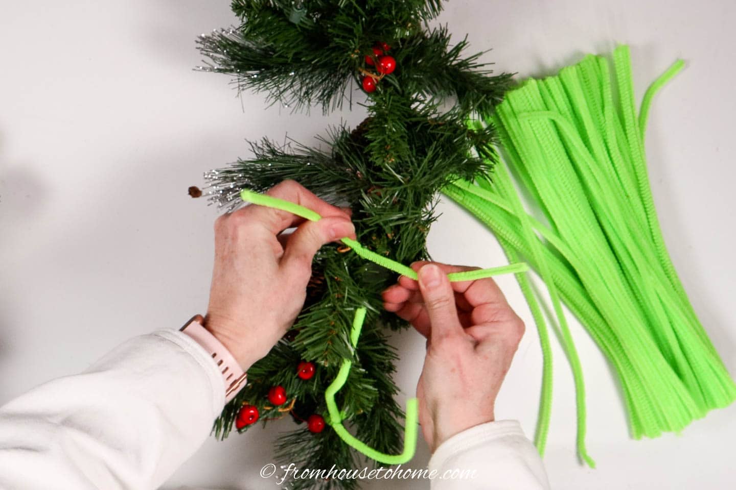 Lime green pipe cleaner being tied on evergreen garland