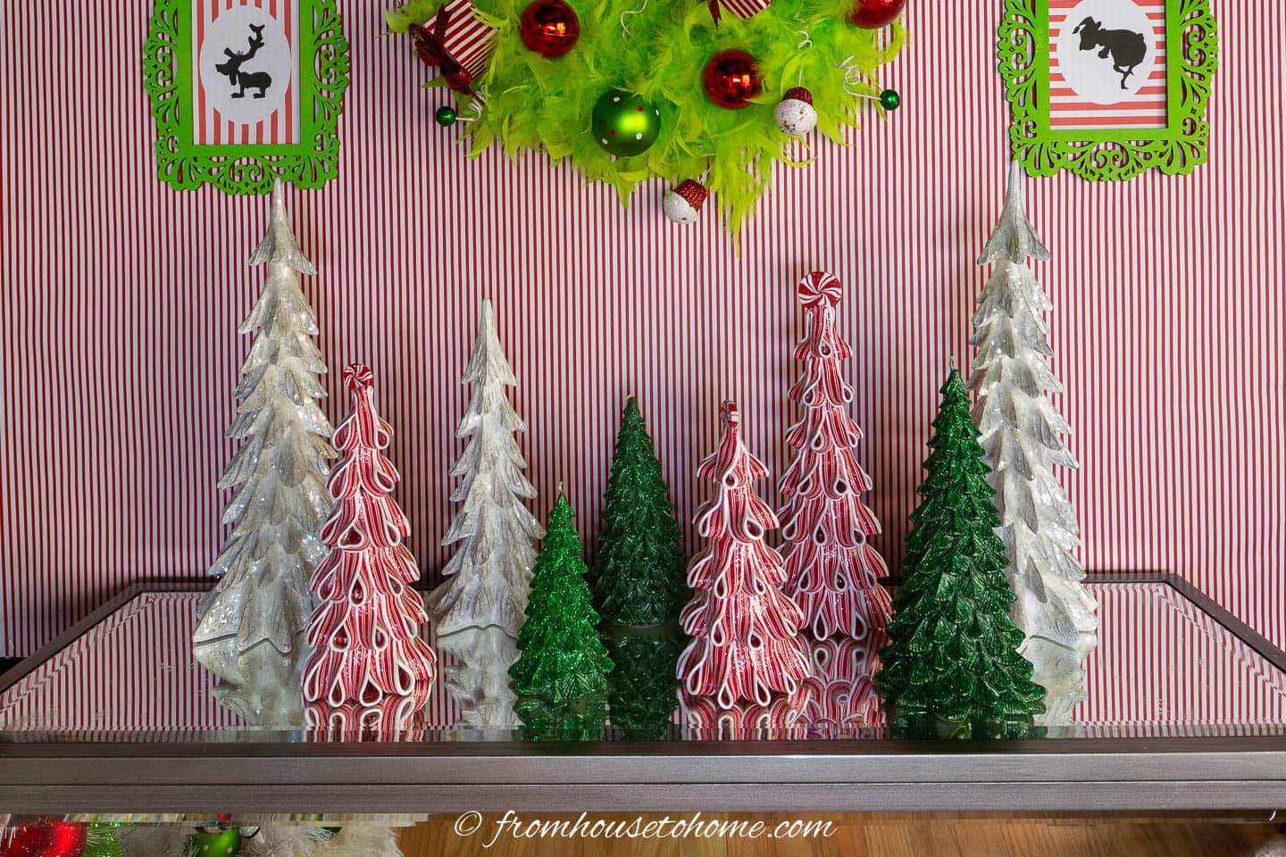 red, white and green mini Christmas trees on a  fireplace mantel underneath a Grinch wreath