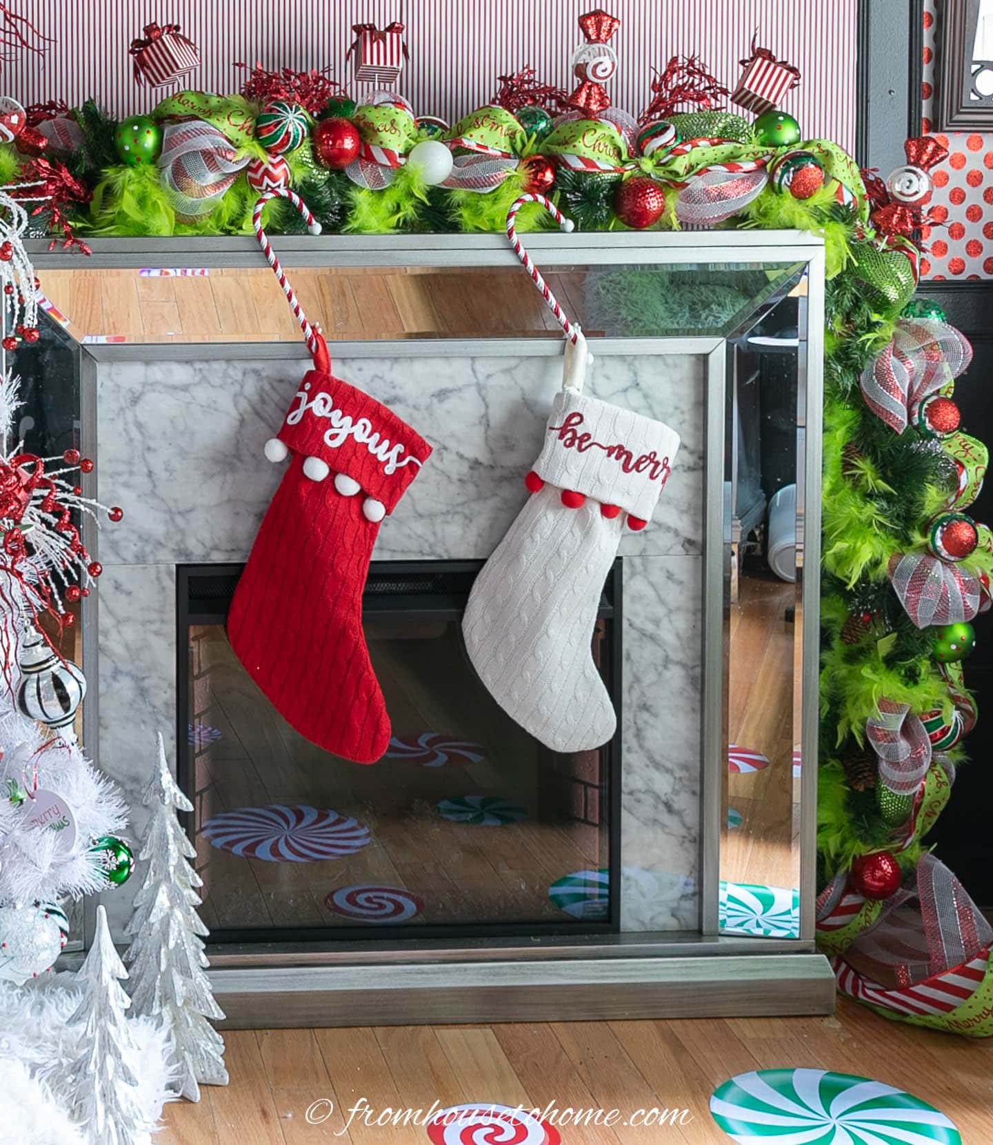red and white stockings hung on a mantel with a Grinch garland