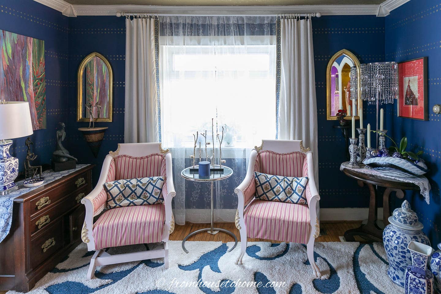 living room with blue walls, white trim, white curtains, two pink and white chairs and lots of blue and white ginger jars
