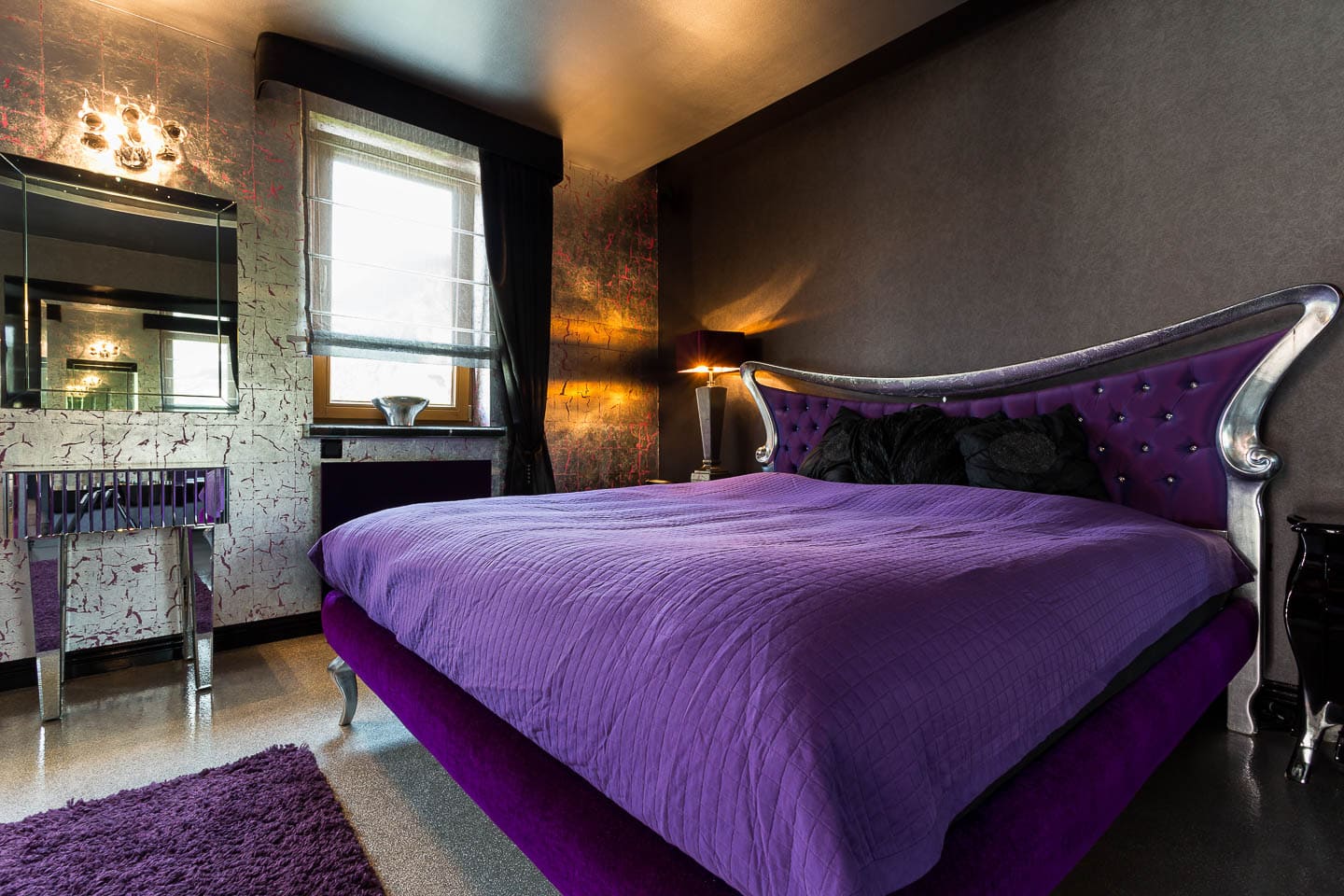 purple and silver bed in front of a dark gray wall