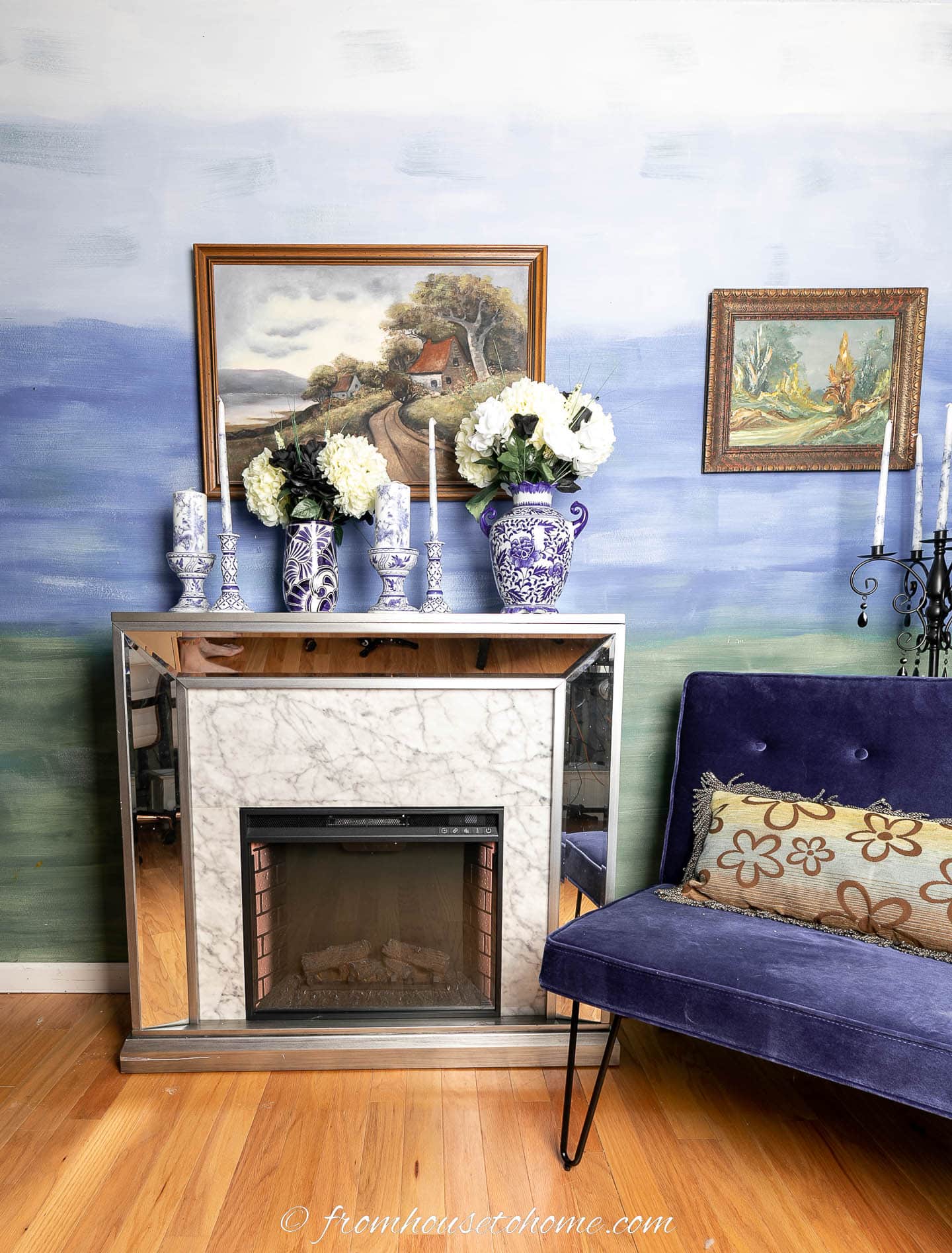 A fireplace and a blue velvet chair in front of a green and blue ombre wall