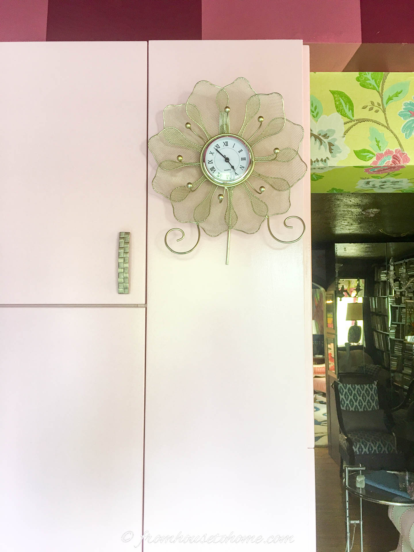 Decorative clock hanging on the side of a light pink kitchen cabinet