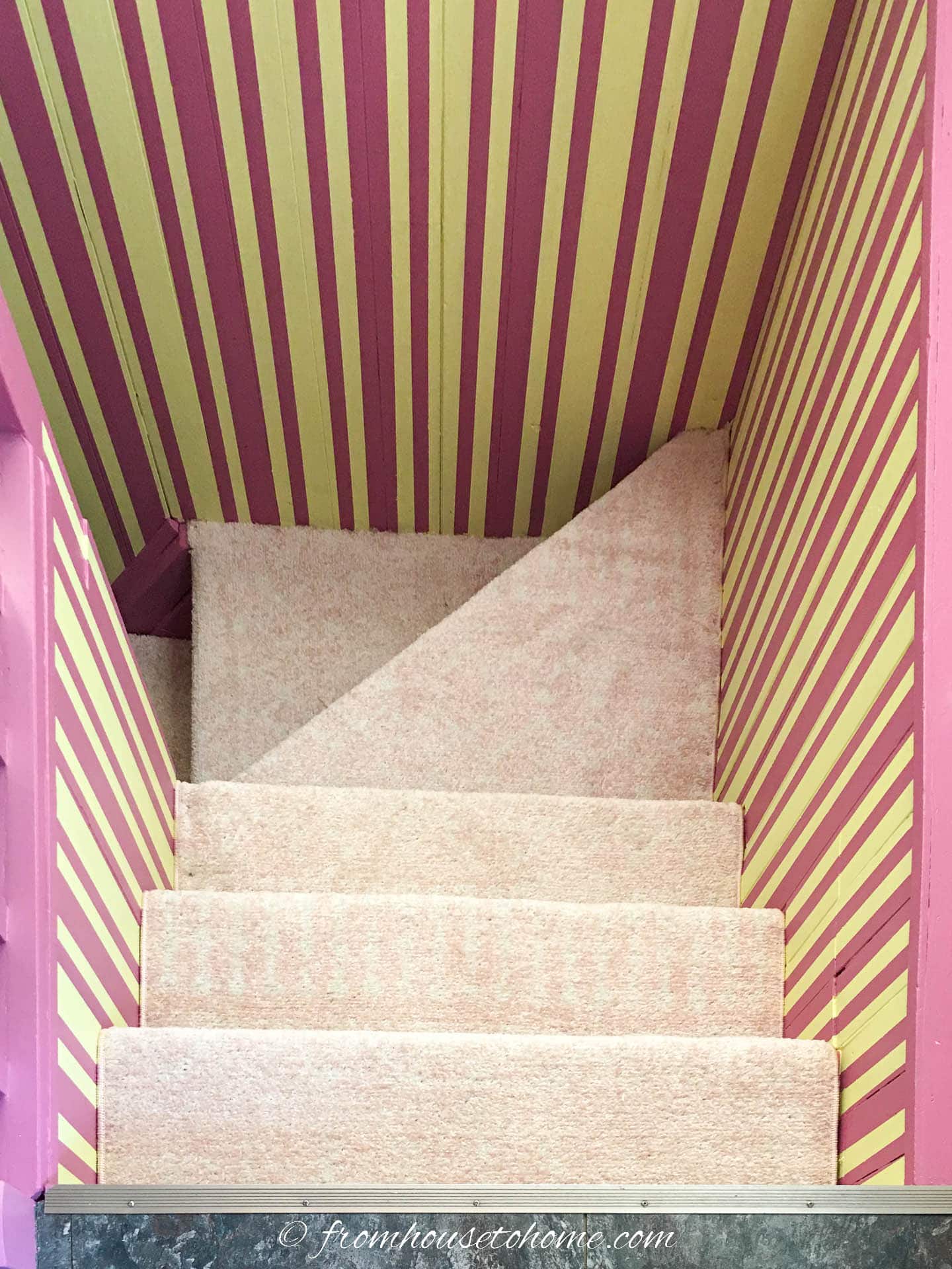 Stairwell with yellow and pink vertical stripes on the walls and light pink carpet on the stairs