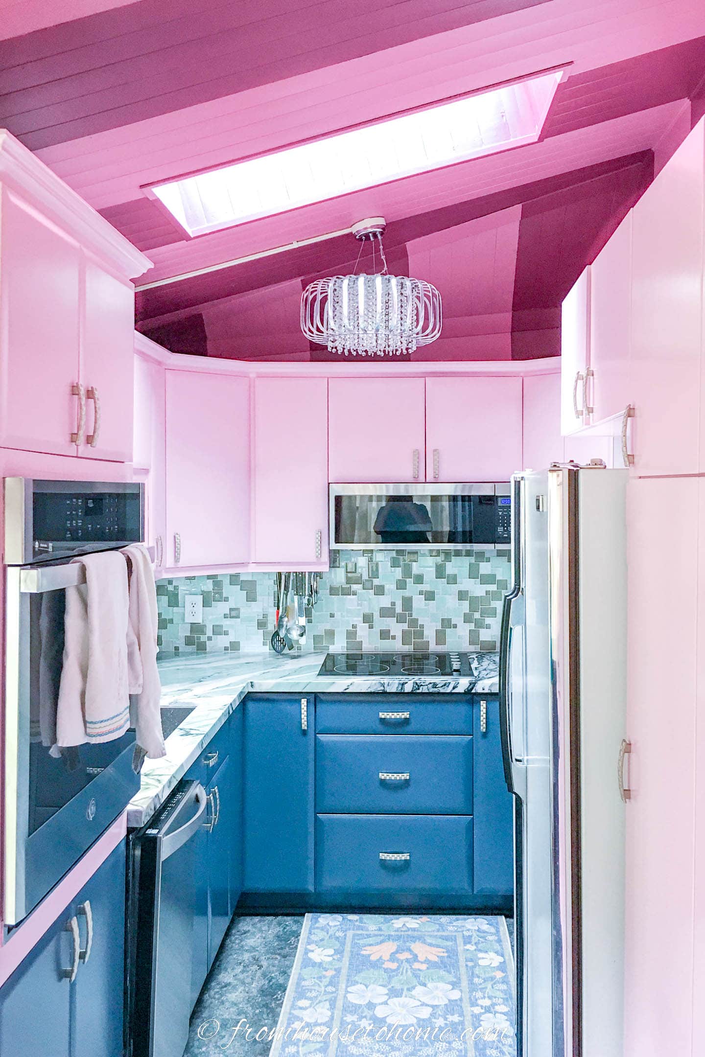 Small galley kitchen finished with pink upper cabinets, teal, white and black countertops, glass mosaic backsplash, and dark teal lower cabinets