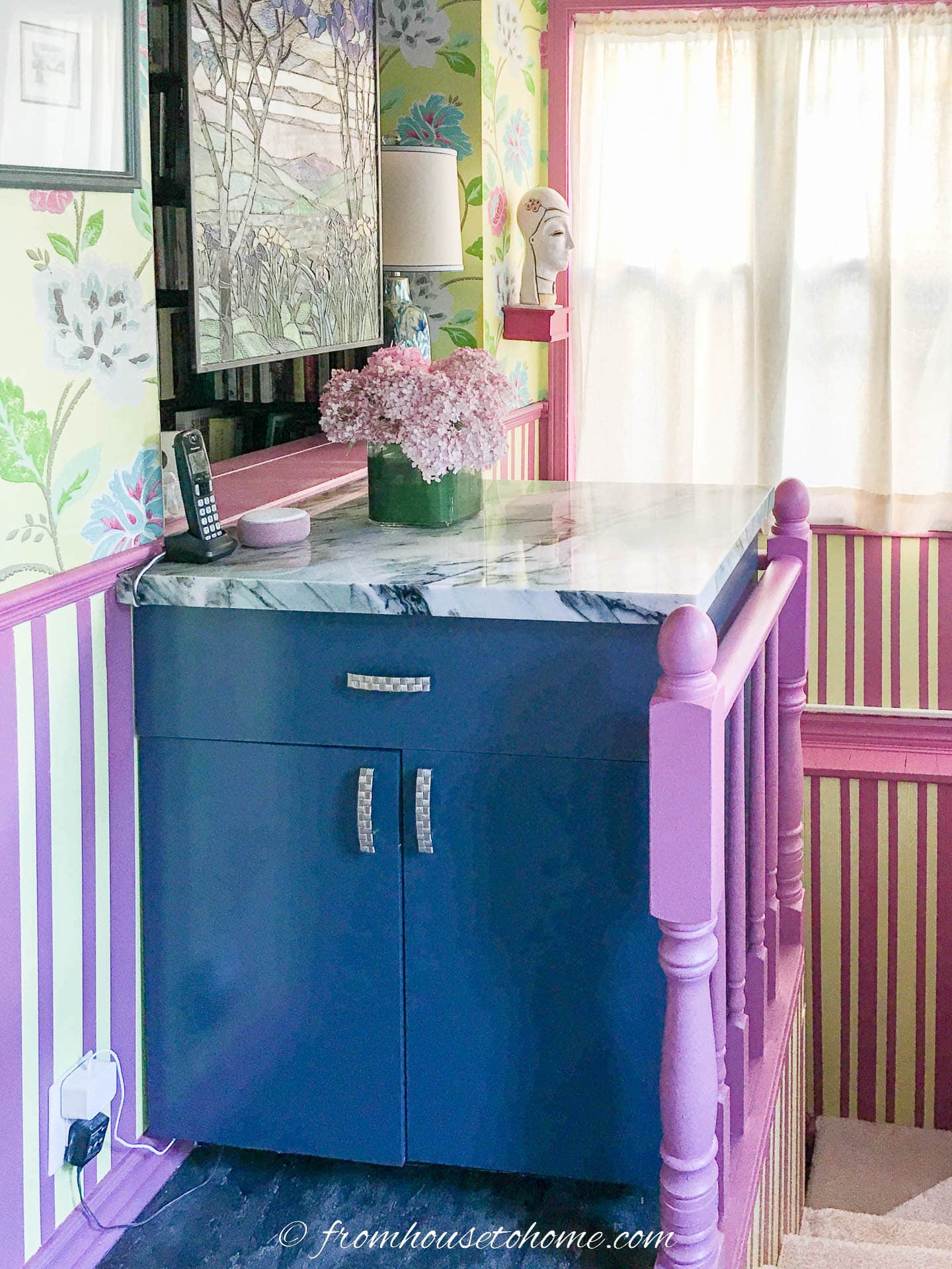 Teal base cabinet installed beside a stairwell with pink woodwork, and painted yellow and pink vertical stripes on the walls