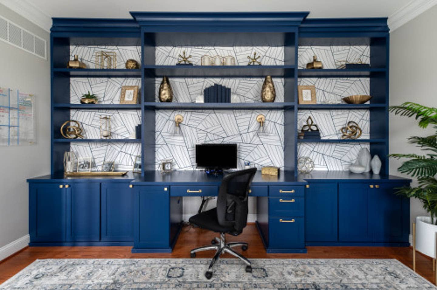 Blue wall-to-wall shelving unit with a built-in desk and a white geometric wallpaper covering the back