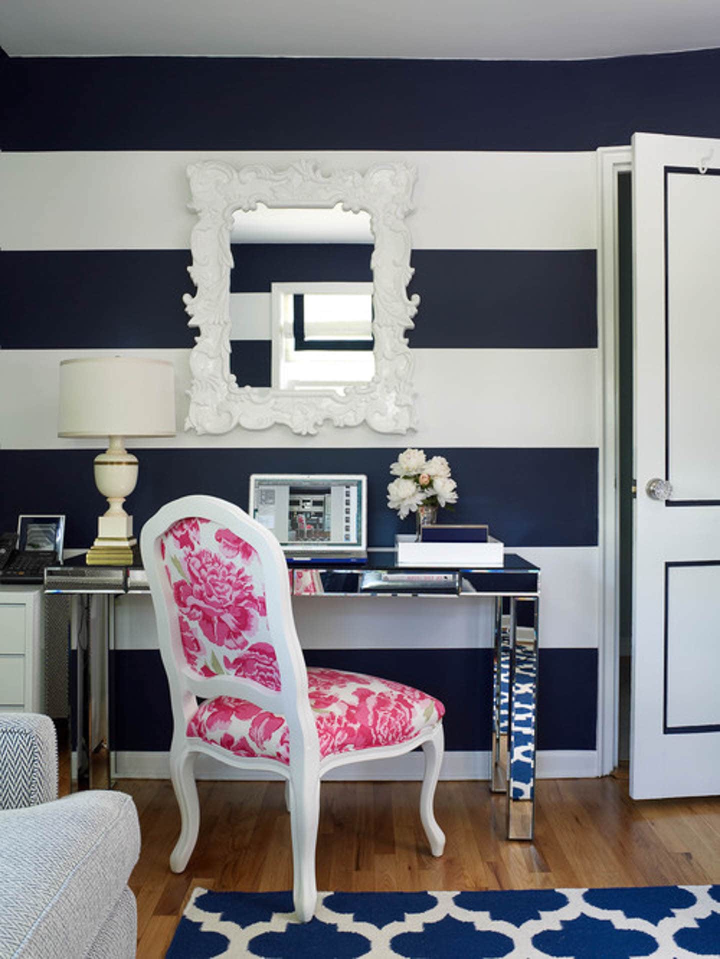 Small home office with wide navy blue and white horizontal stripes, a mirror desk, blue and white area rug and a bright pink and white chair