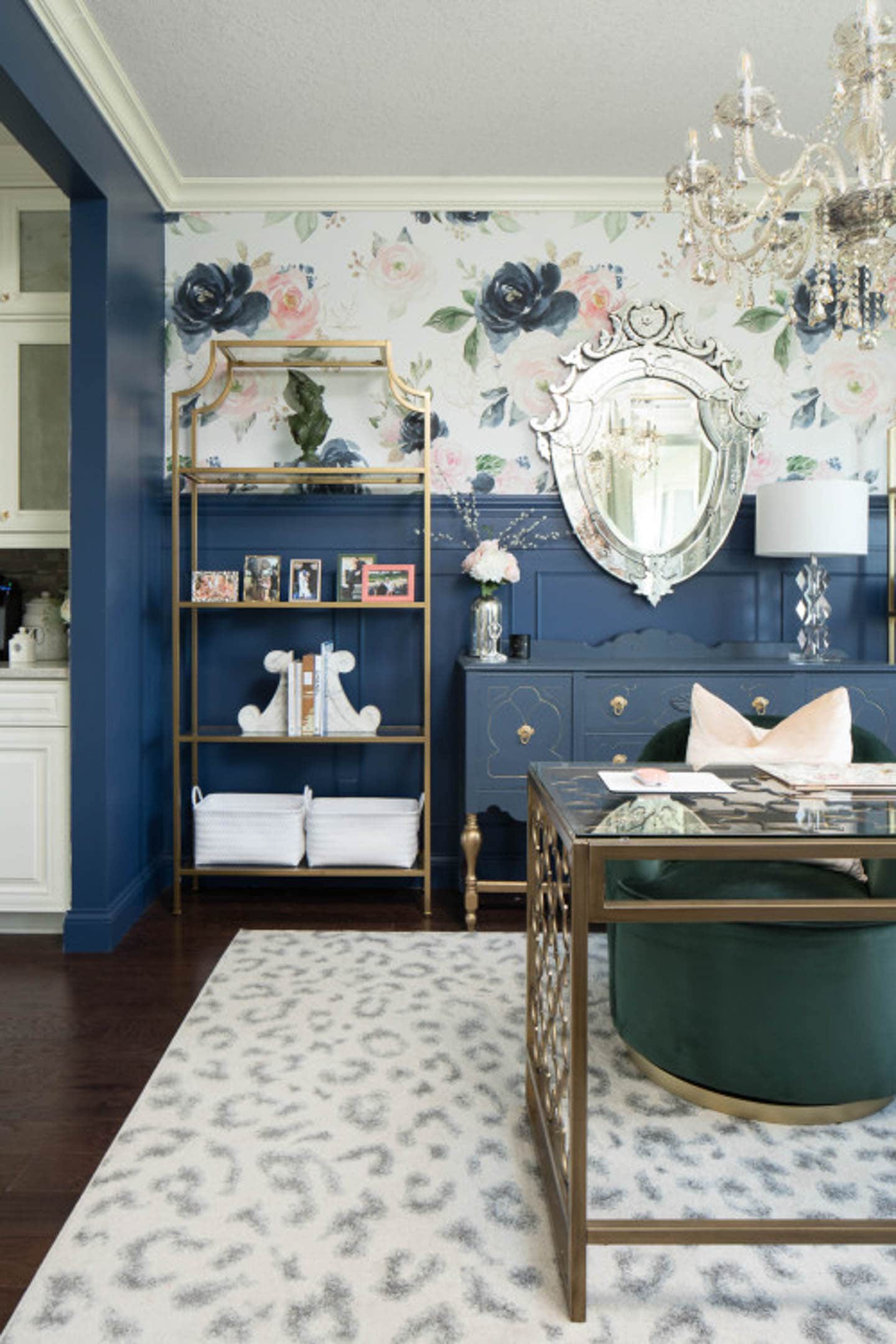 Glam home office with dark blue wainscoting, a pink and blue mural above, a gold etagere and Venetian mirror behind a gold desk