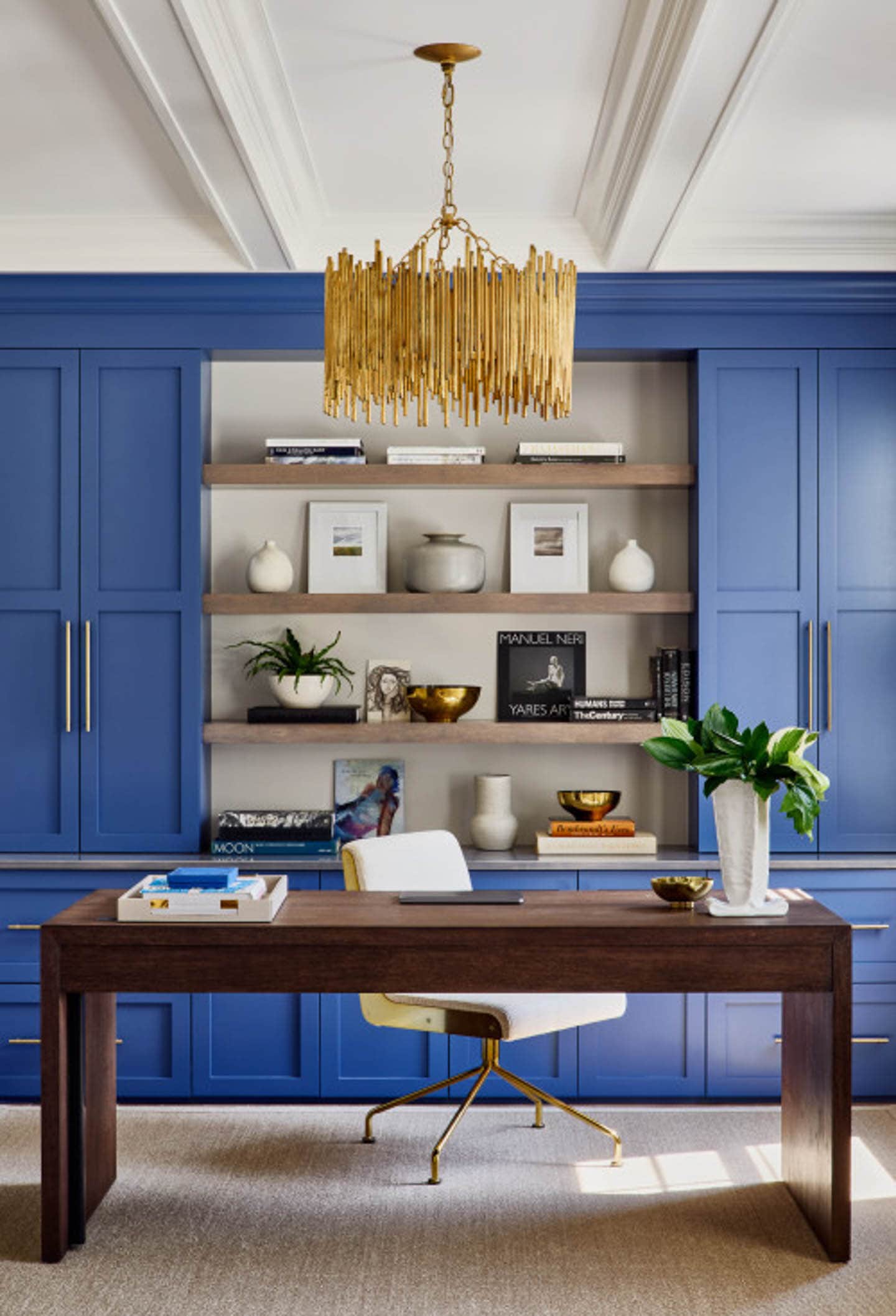 Wood desk in front of royal blue cabinets with a large gold chandelier hanging from the ceiling