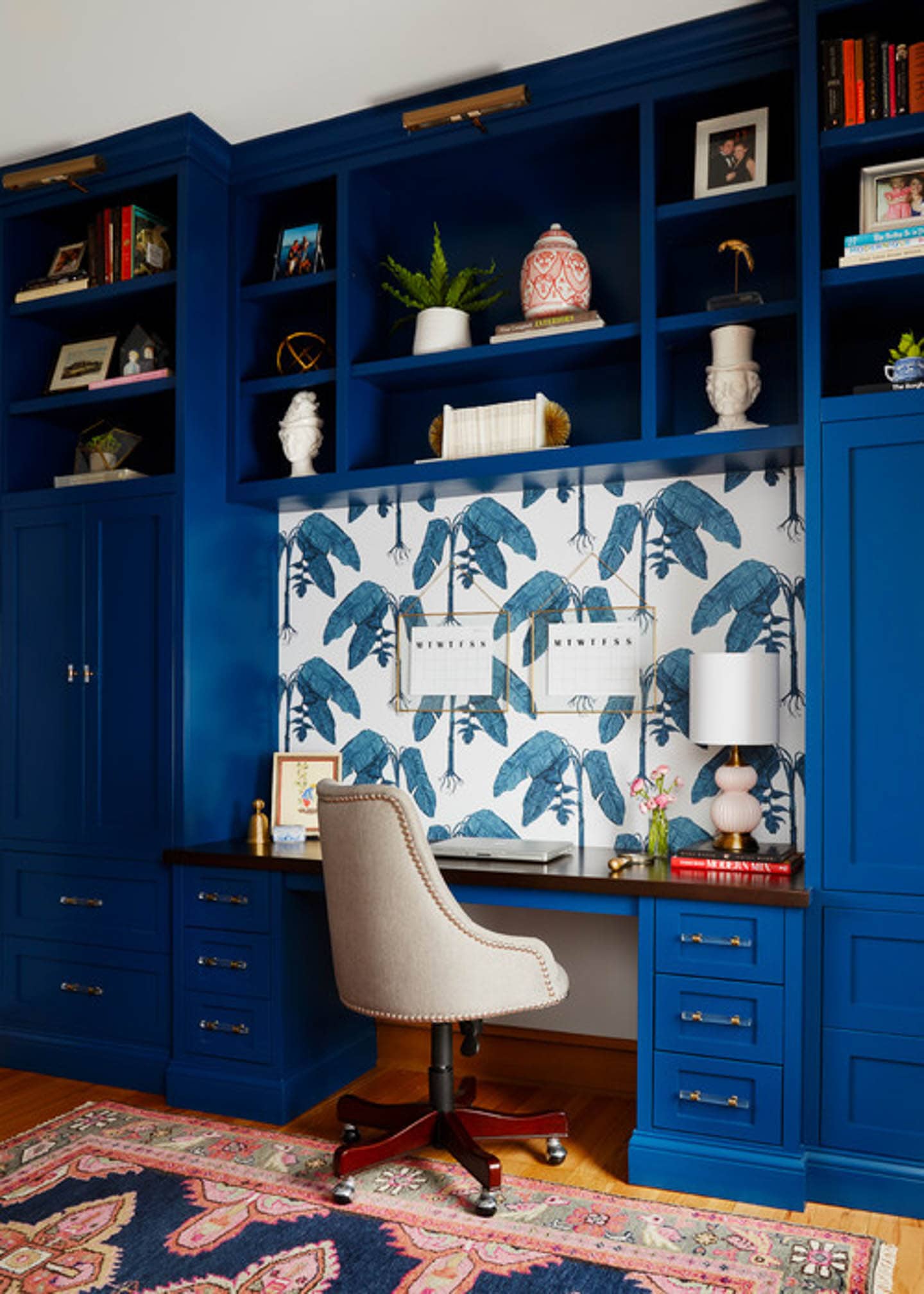 Dark blue shelves with a built-in desk and a white and blue leaf wallpaper above it